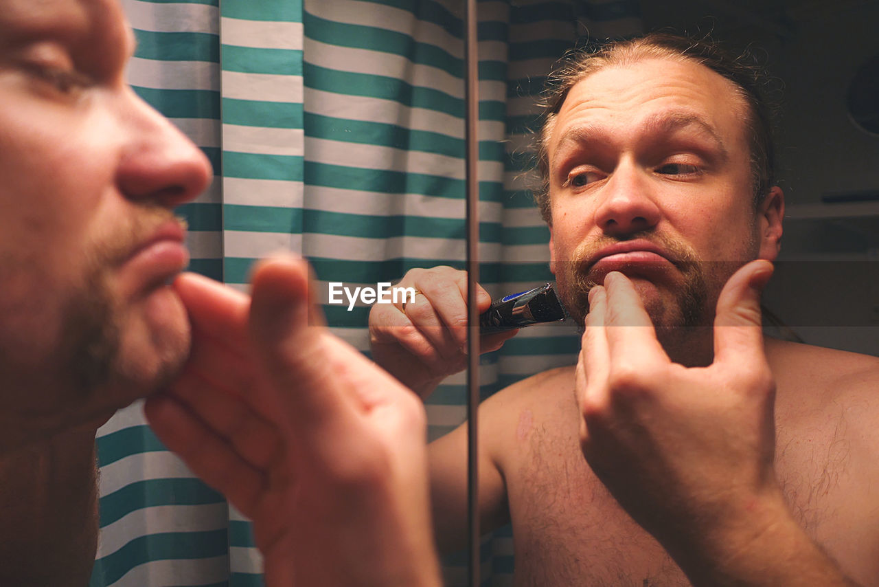 Reflection of man in mirror shaving in bathroom