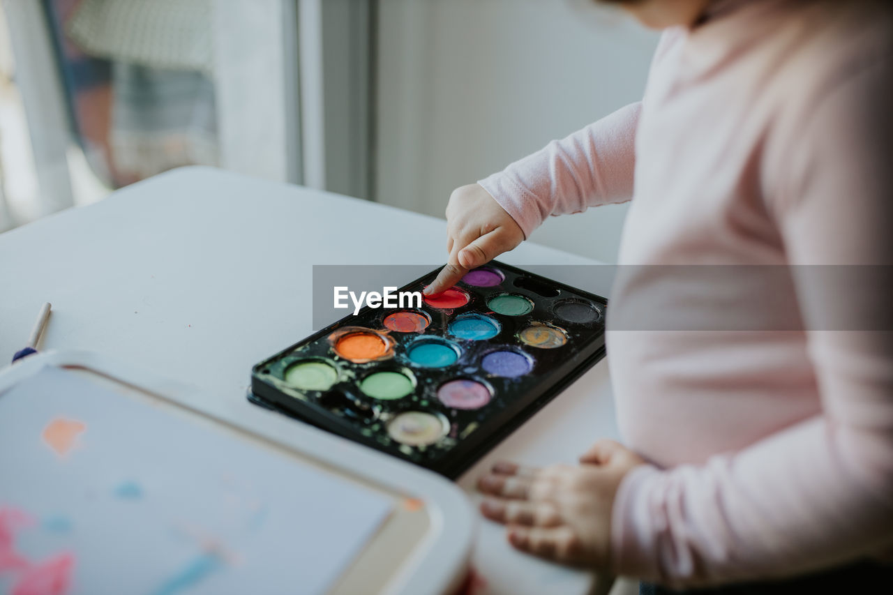 Midsection of girl touching paint in palette