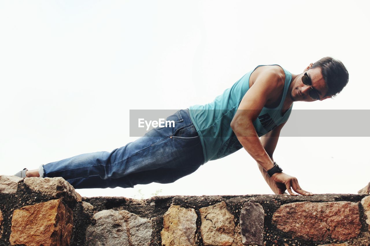 SIDE VIEW OF YOUNG MAN WEARING SUNGLASSES ON ROCK