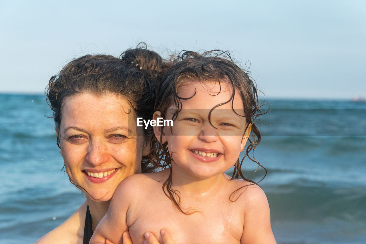 Portrait of smiling mother and daughter against sea