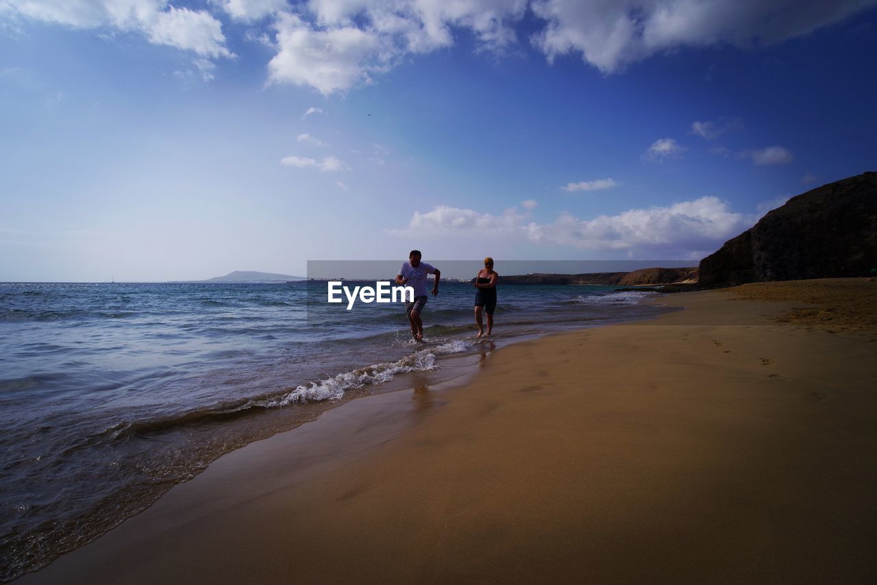 Couple running on shore at beach against sky