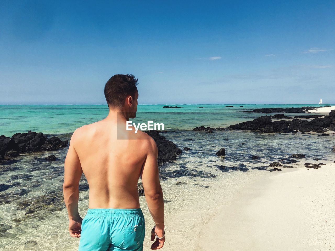 REAR VIEW OF SHIRTLESS MAN LOOKING AT SEA