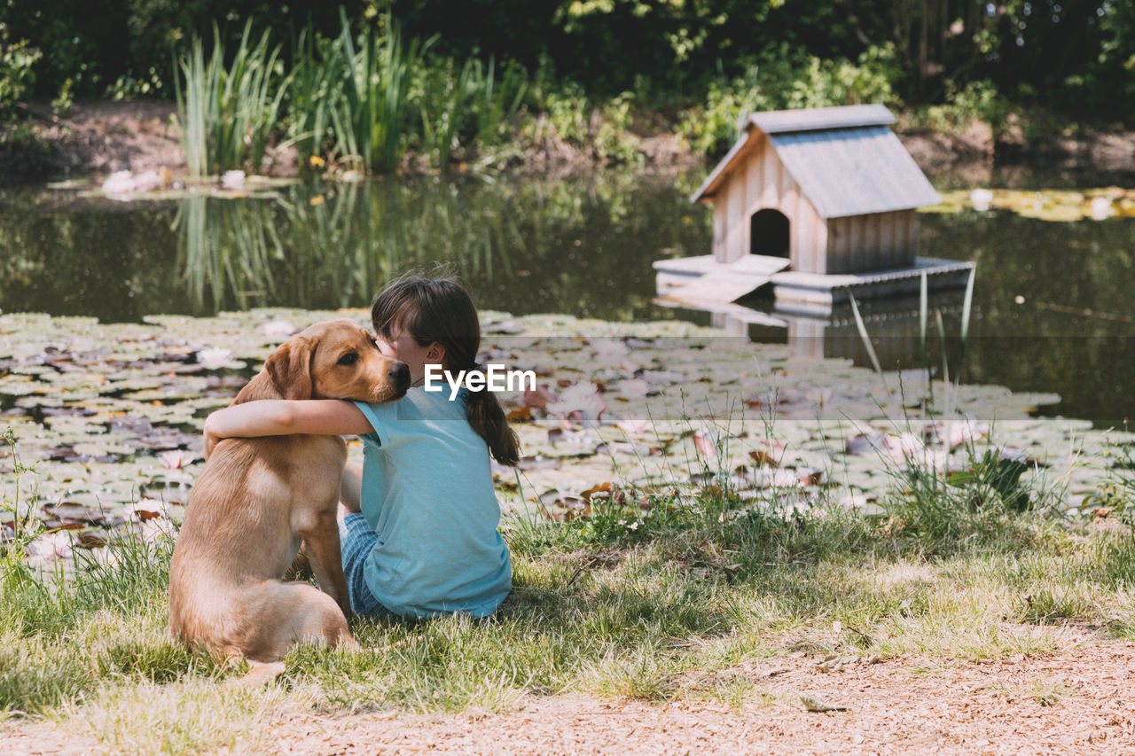 Friendship of animals and children, people.  girl sits on the bank of a pond and hugs a labrador 