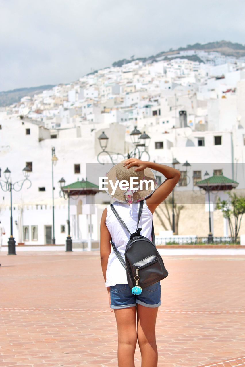 Rear view of girl with backpack looking at buildings