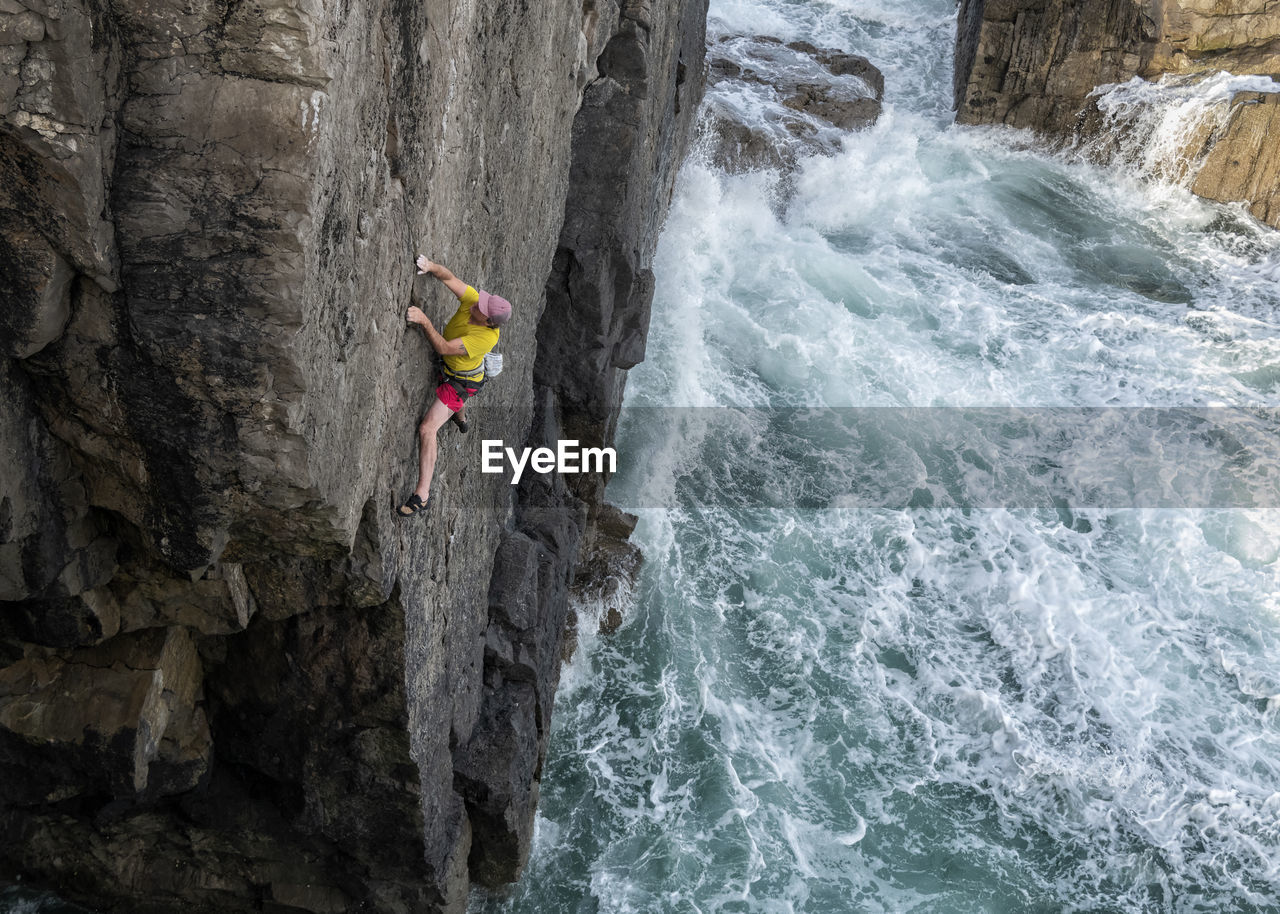 Mature male rock climber climbing up cliff against sea