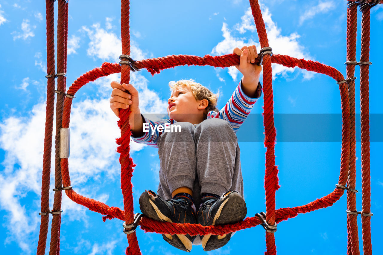 Low angle view of boy balancing on rope against sky in playground