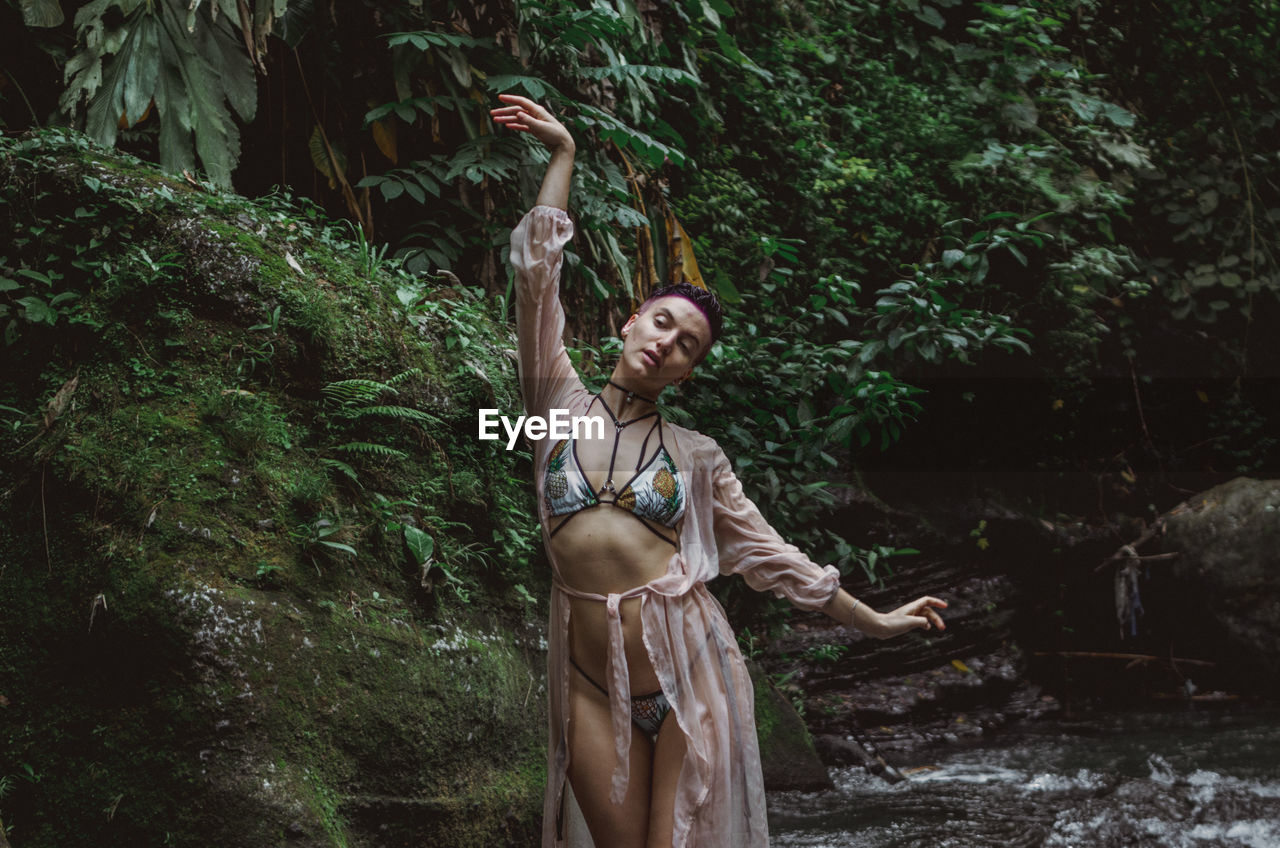 Woman with arms raised standing against tree in forest