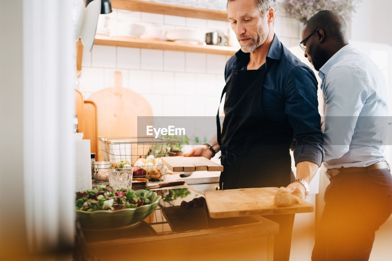 Mature man working at counter while standing with friend in kitchen