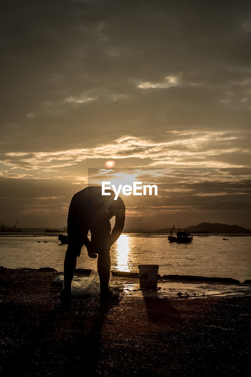 Silhouette fisherman with net on jetty at sea