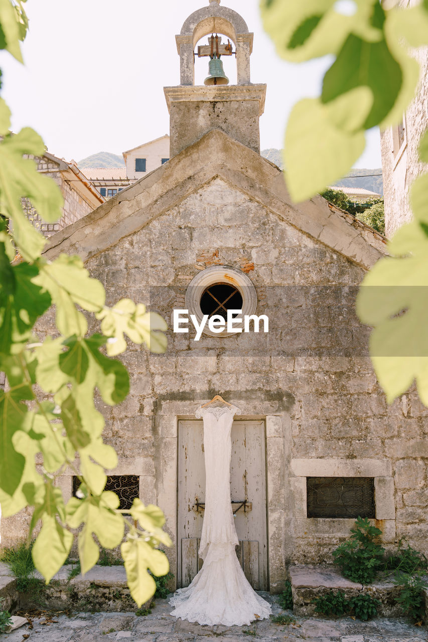 LOW ANGLE VIEW OF CROSS AMIDST PLANTS AGAINST BUILDING