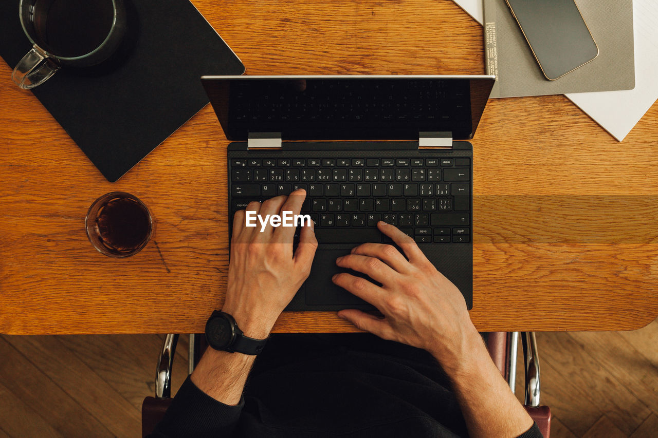 High angle view of man using laptop on table, home office, using technology, coffee and smart watch.