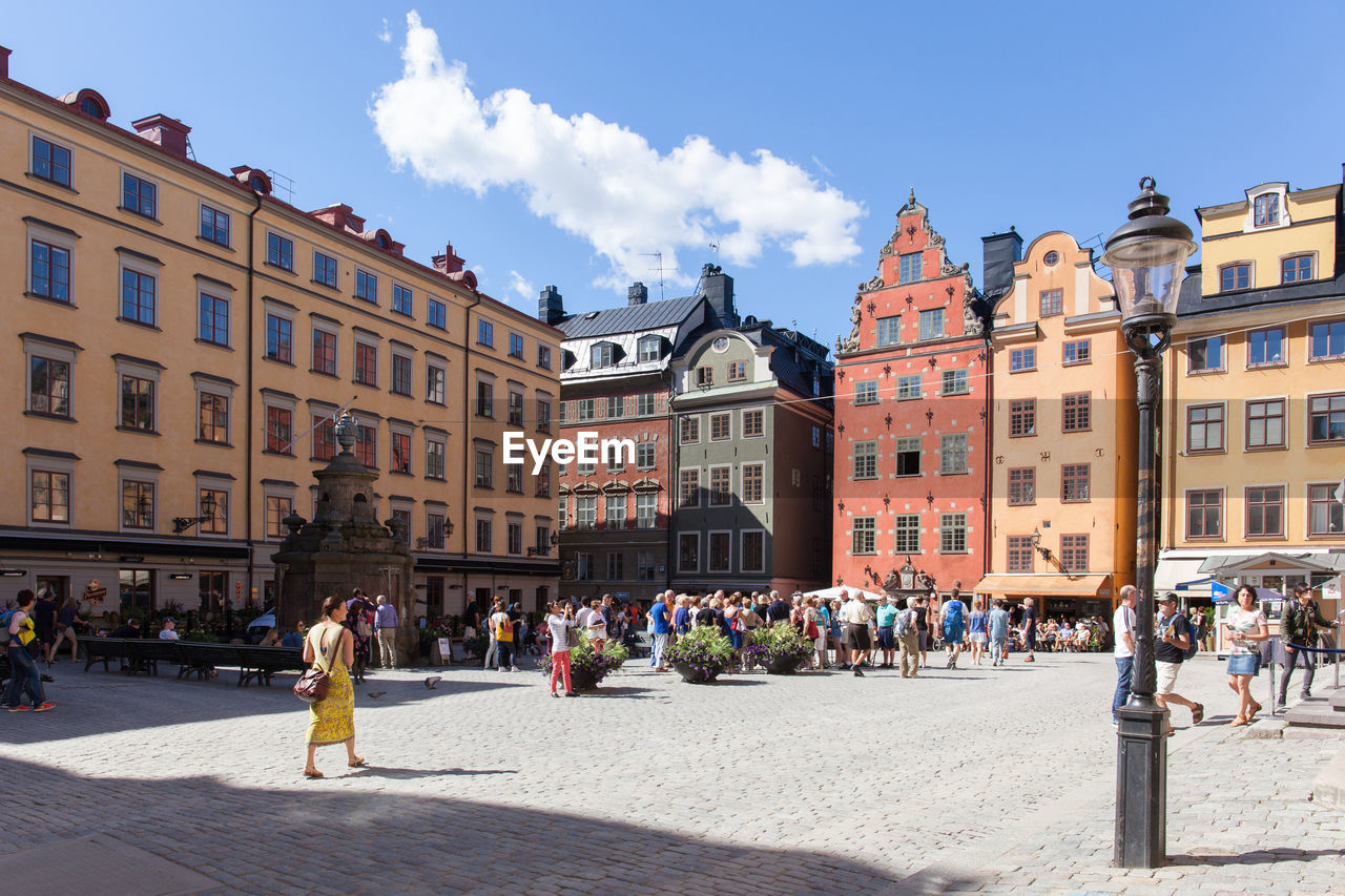 Crowd in town square by buildings against sky