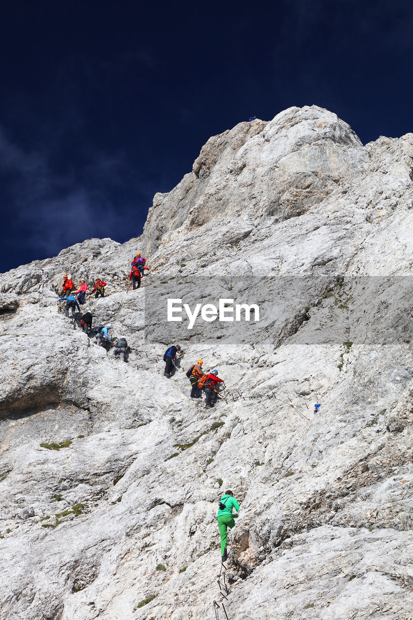 Low angle view of people climbing on mountain against sky