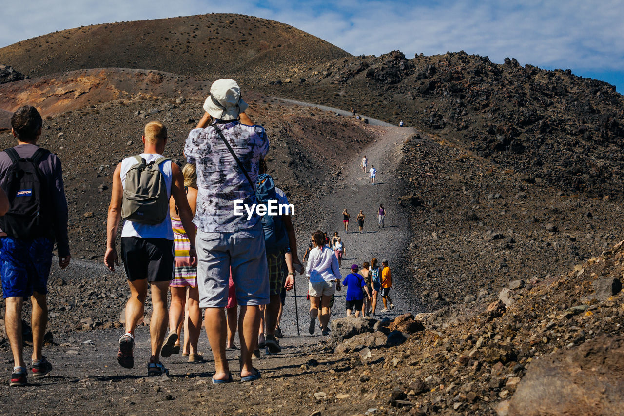 Rear view of people walking on dirt road during sunny day