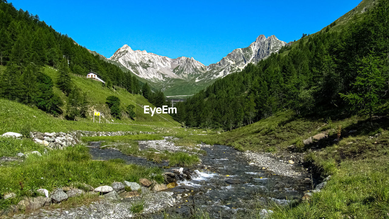 Scenic view of stream by mountains against clear sky