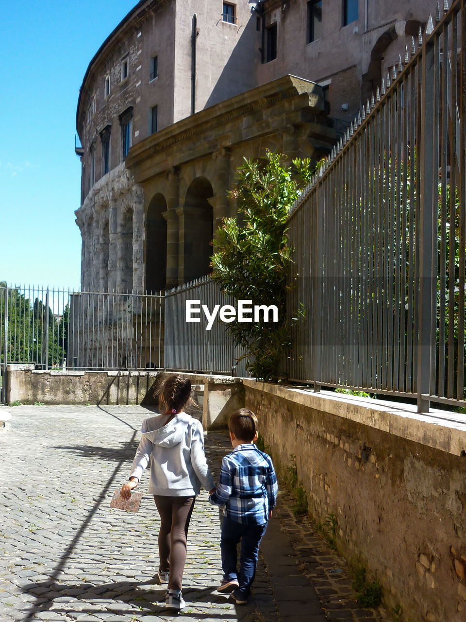 Two children walking in the historic center of rome. the little girl guides her younger brother. 