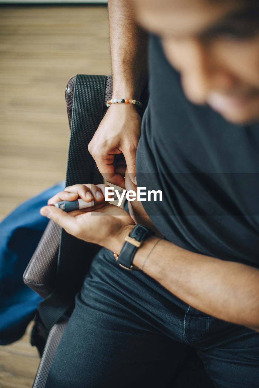 High angle view of businessman injecting insulin in abdomen while sitting in office