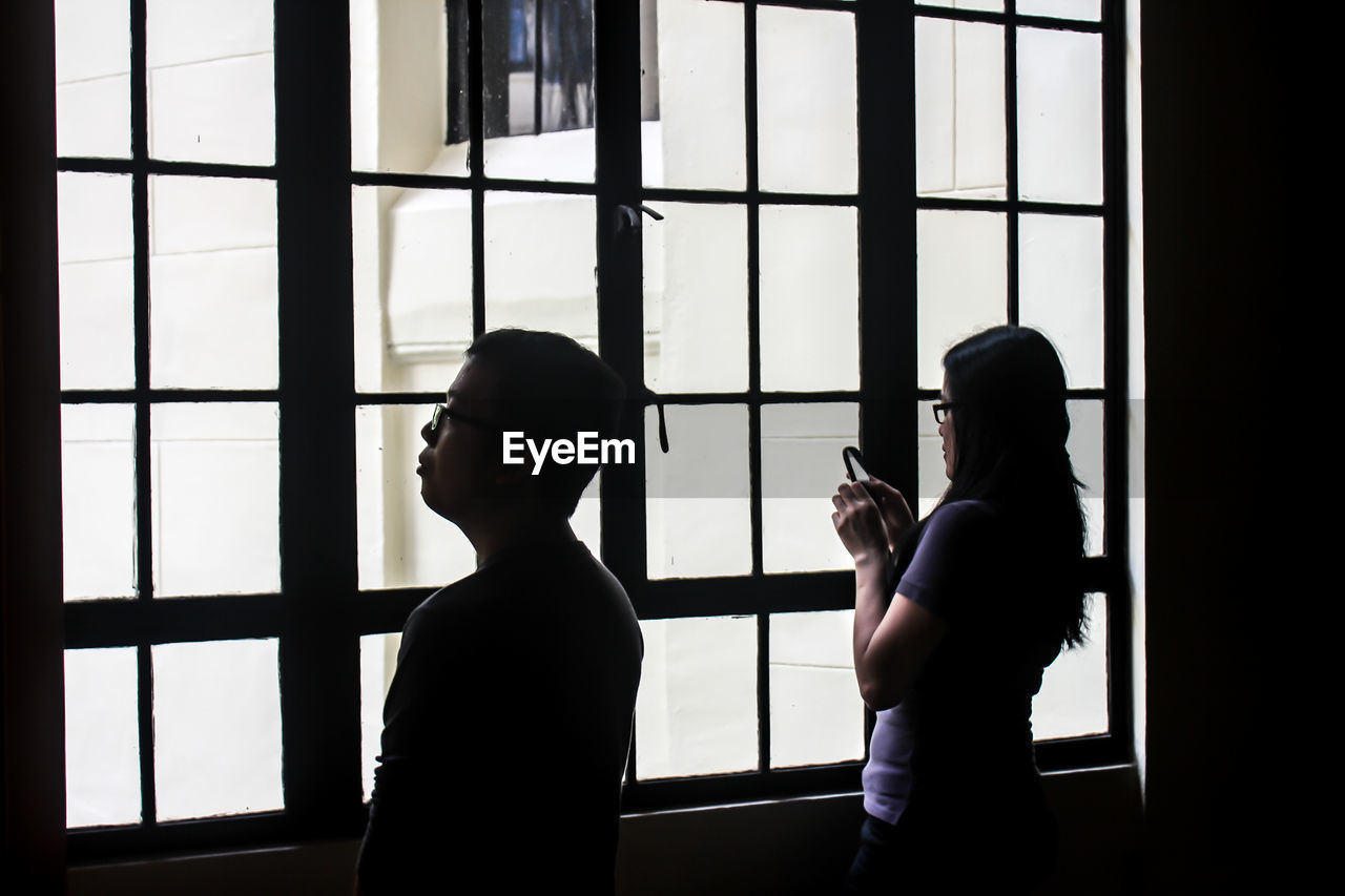 Man looking by woman using phone in front of building window