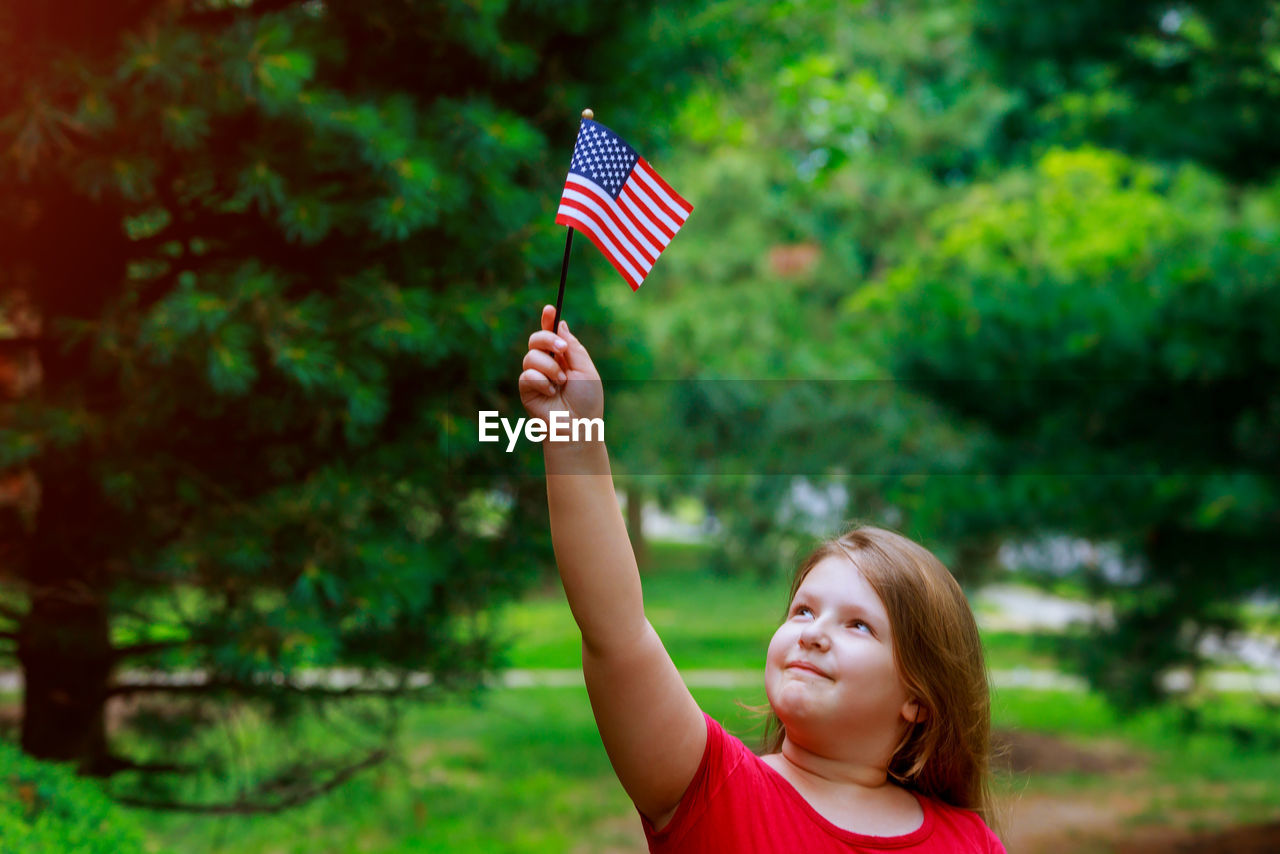 Cute overweight girl with small american flag standing at public park