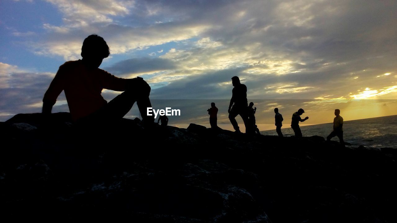 SILHOUETTE PEOPLE ON ROCKS AT BEACH DURING SUNSET