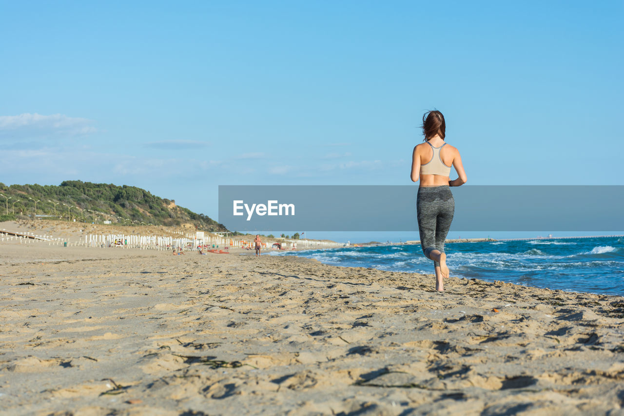 Rear view of woman running on beach against sky