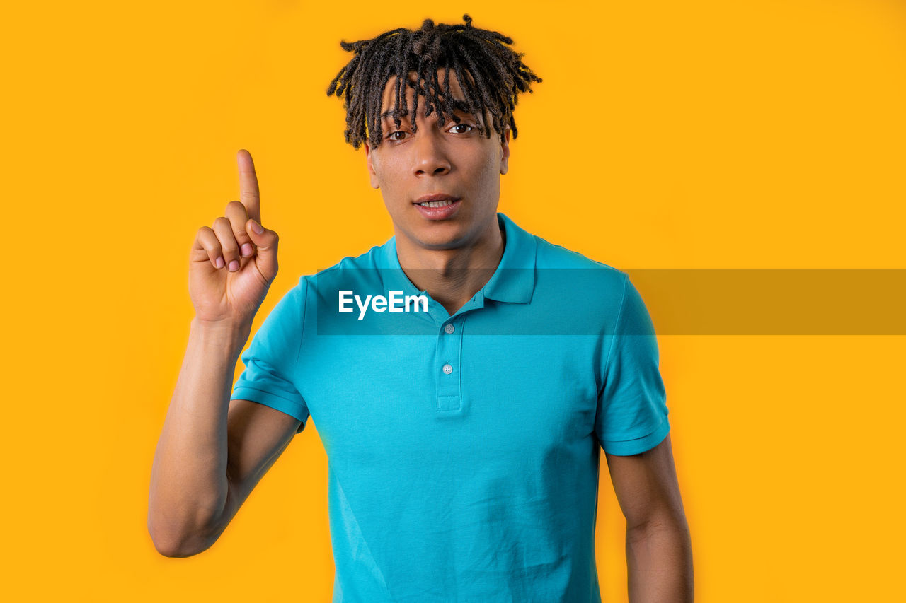 one person, colored background, studio shot, yellow, adult, polo shirt, waist up, portrait, yellow background, young adult, men, indoors, front view, casual clothing, emotion, orange color, standing, copy space, person, orange background, t-shirt, clothing, blue, looking at camera, smiling, hairstyle, lifestyles, holding, happiness