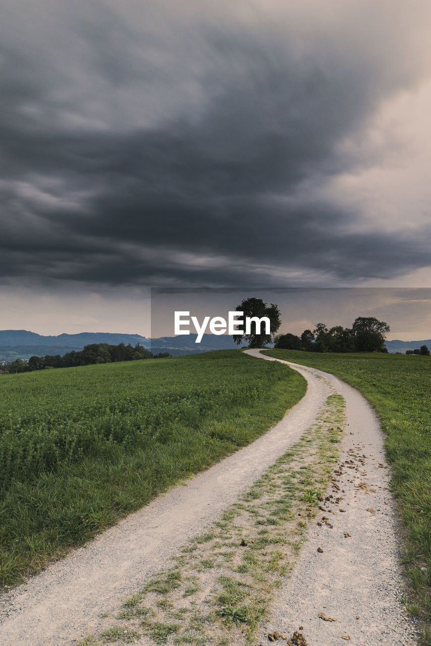 cloud, sky, environment, landscape, plant, land, nature, road, horizon, grass, dramatic sky, beauty in nature, scenics - nature, field, rural area, storm, the way forward, storm cloud, rural scene, no people, dirt road, cloudscape, footpath, tranquility, overcast, tree, transportation, hill, prairie, dirt, outdoors, moody sky, non-urban scene, grassland, plain, tranquil scene, sunset, coast, green, diminishing perspective, travel, agriculture, atmospheric mood, dusk, vanishing point, soil, water, day, travel destinations, sea, sunlight, street