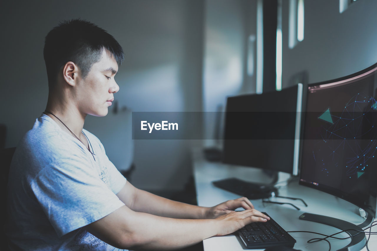 Side view of young man using computer while sitting on table