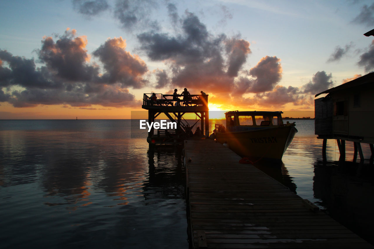 Boats moored by pier in sea during sunset