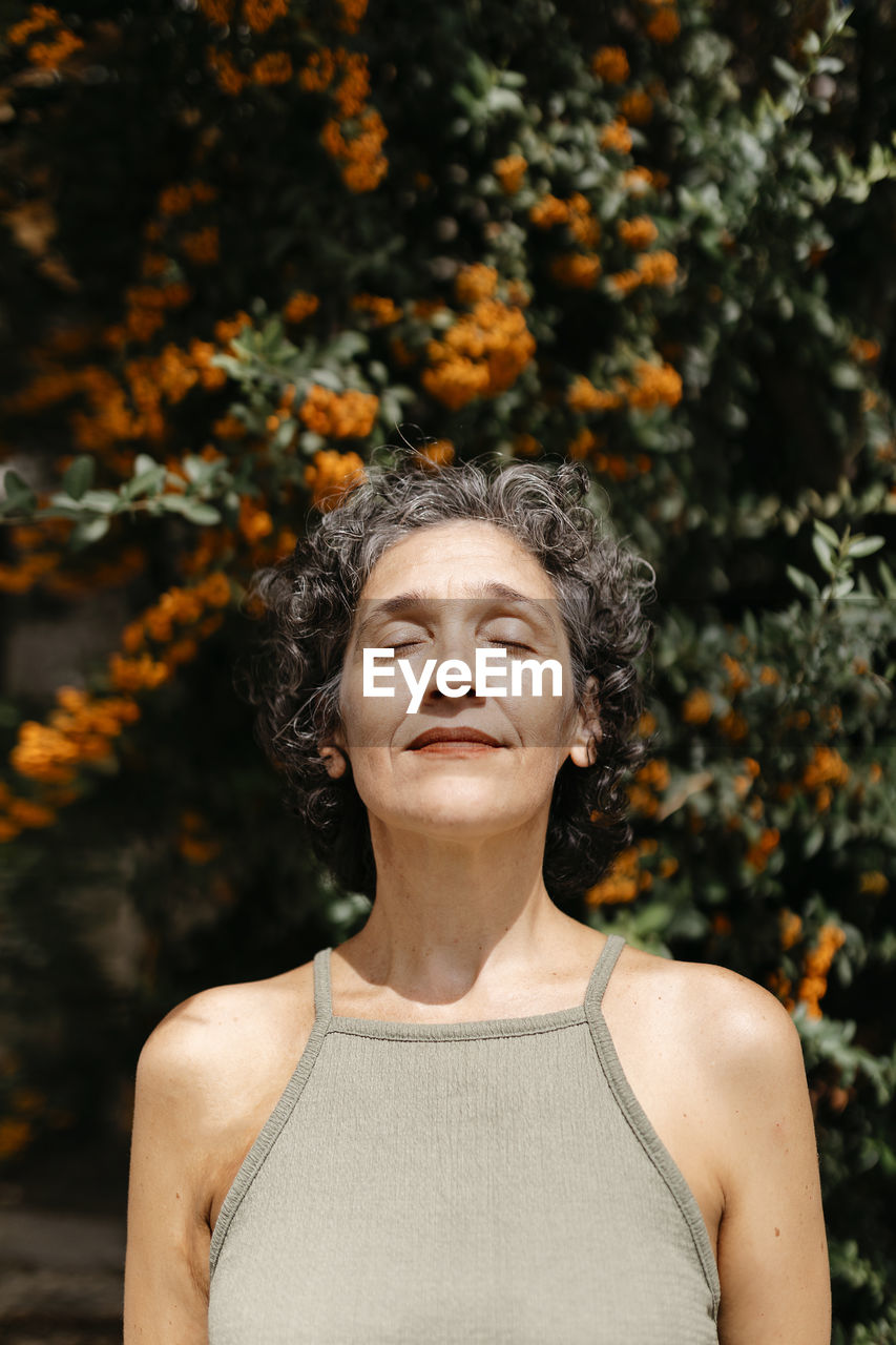 Contemplating mature woman standing against orange tree