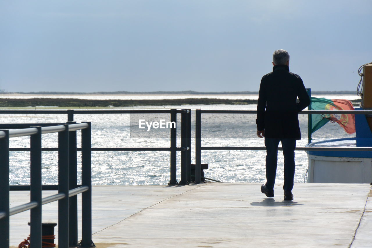 Rear view of man walking on pier over sea against clear sky