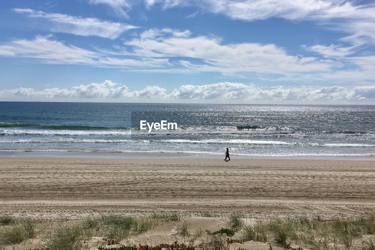 WOMAN STANDING ON BEACH AGAINST SKY