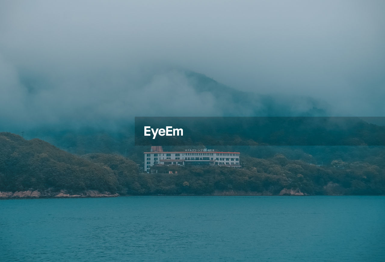 SCENIC VIEW OF SEA BY BUILDINGS AGAINST MOUNTAIN