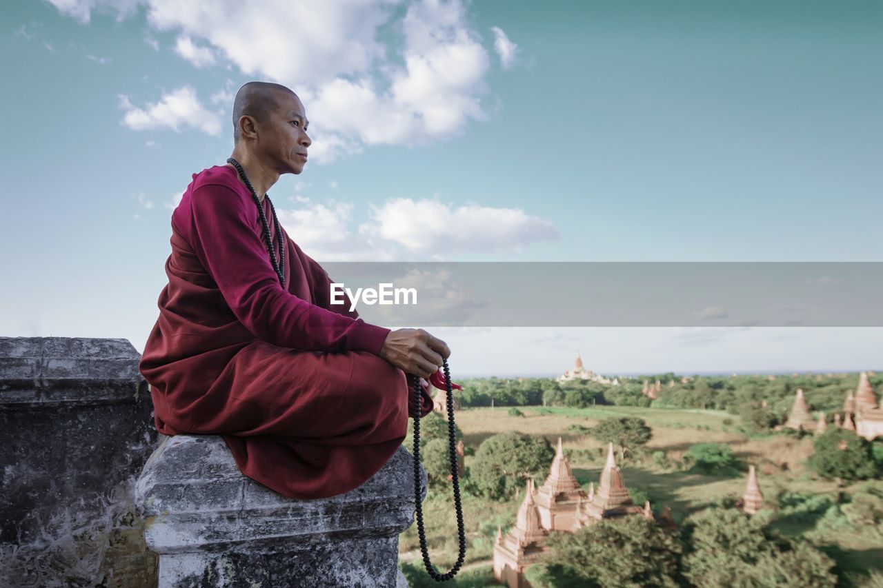 LOW ANGLE VIEW OF MAN SITTING ON ROCK AGAINST SKY