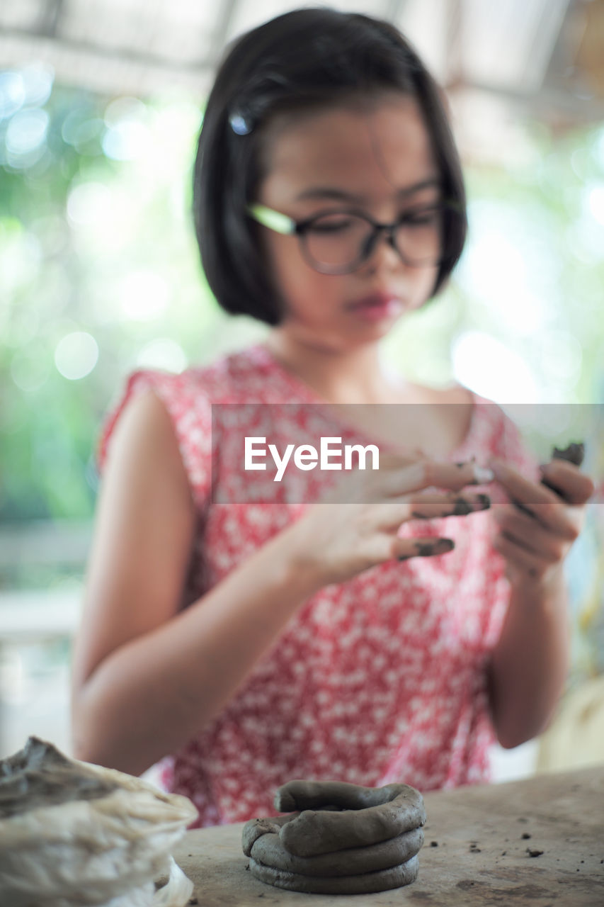 MIDSECTION OF WOMAN HOLDING EYEGLASSES WHILE SITTING IN TABLE