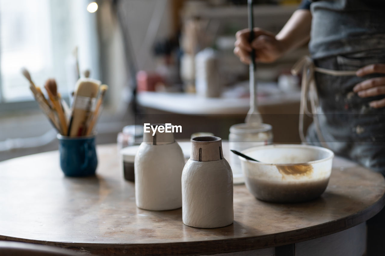 Crop photo of master leaving clay vases to dry out on round table in shop closeup