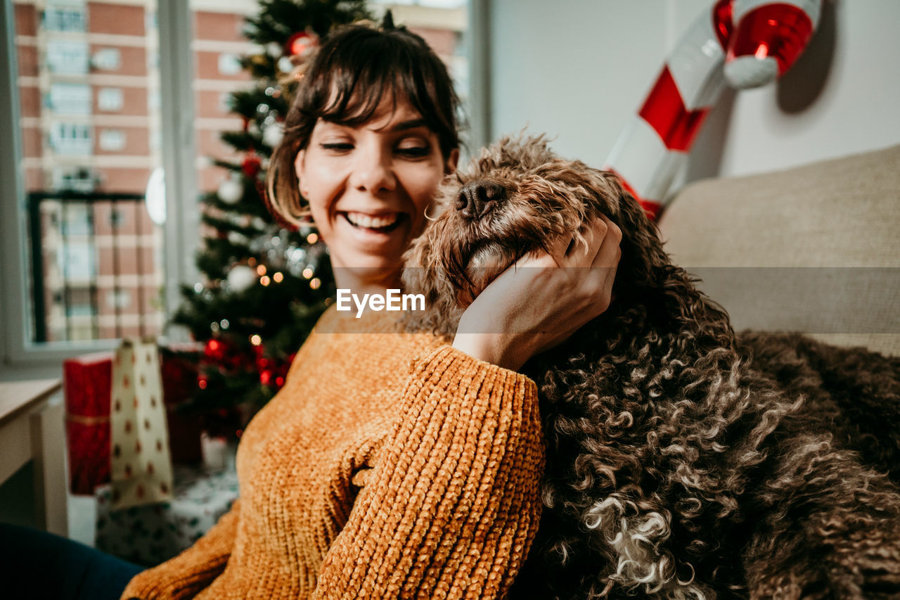 PORTRAIT OF SMILING YOUNG WOMAN WITH DOG AT HOME