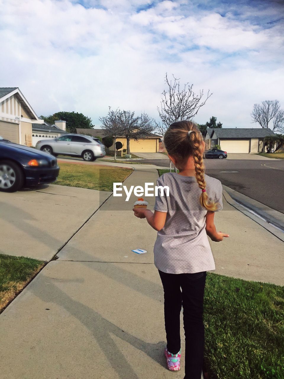 Rear view of girl holding cupcake while walking on sidewalk