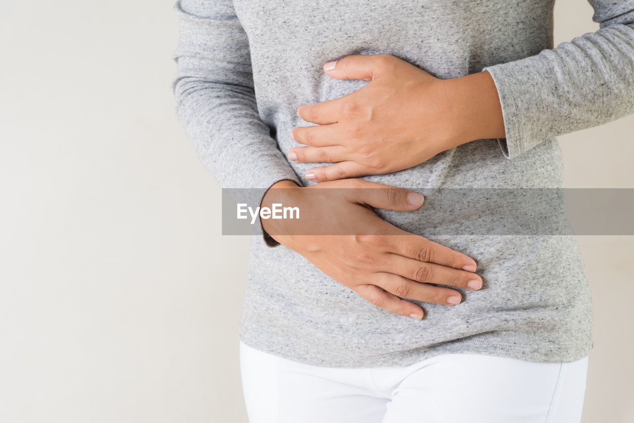 Midsection of woman with stomachache standing against gray background