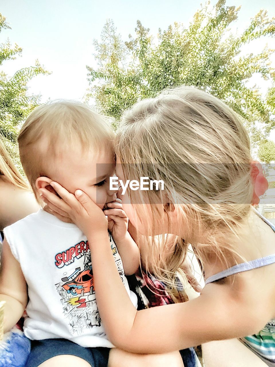 Close-up of girl with brother against tree