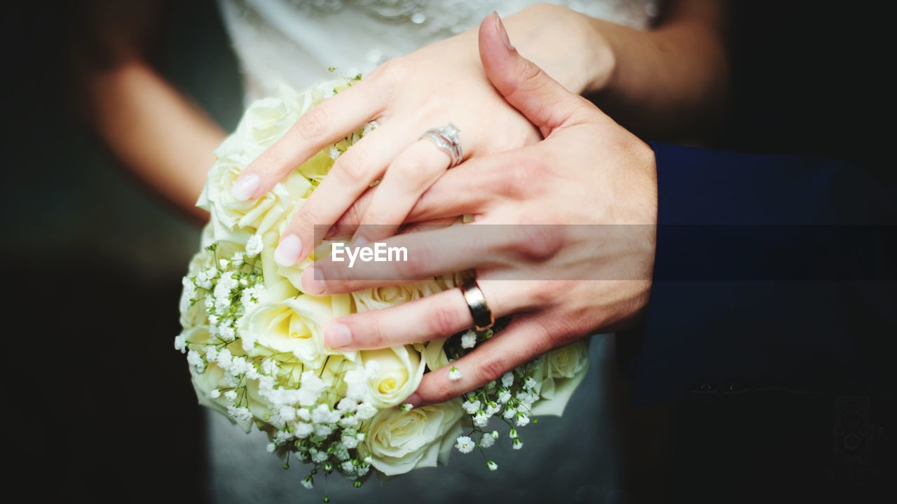Cropped hands of bride and groom holding white rose bouquet