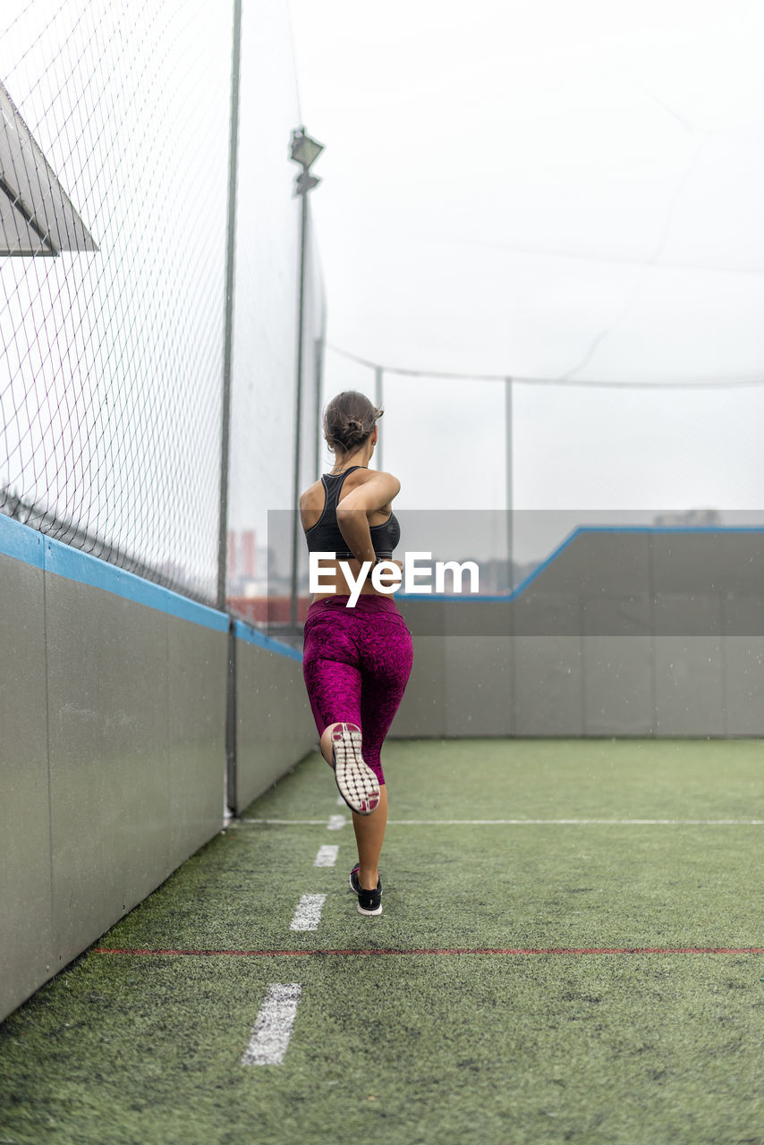 Full body of enduring female athlete in activewear running above ground during intense training in stadium