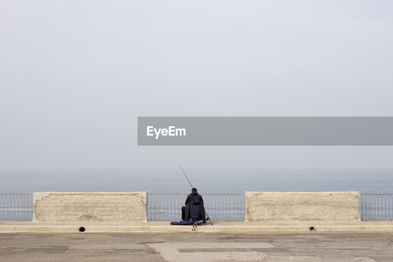 Rear view of person fishing at promenade against sky during foggy weather