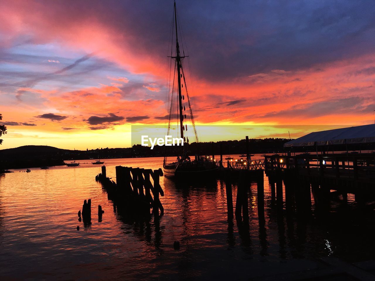 Silhouette boats moored at harbor against sky during sunset