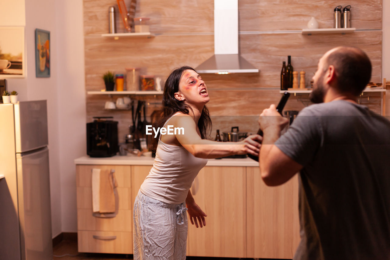 portrait of young woman using mobile phone while standing in kitchen