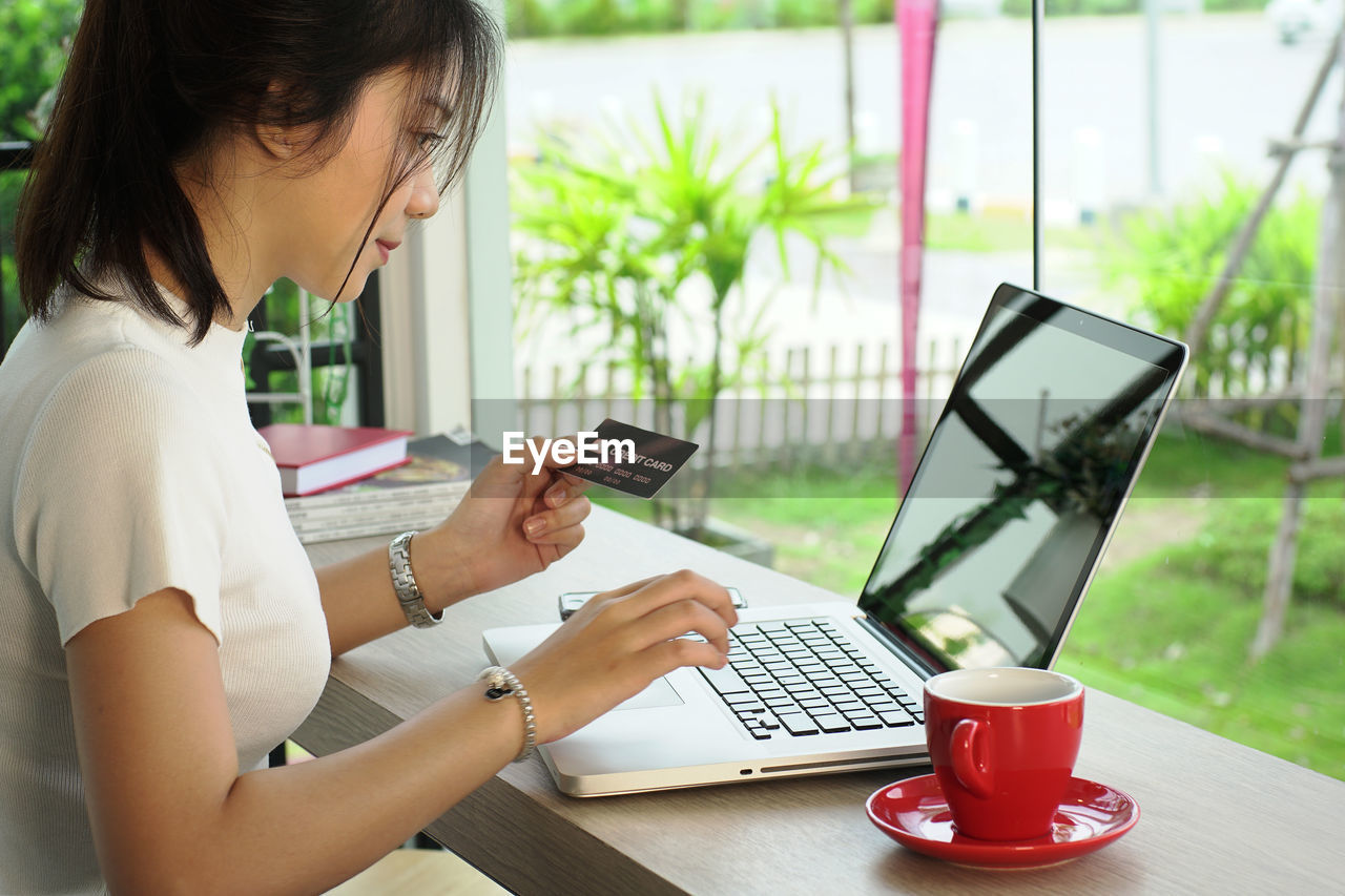 Young woman holding credit card while using laptop at home