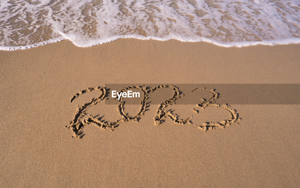 Hand-drawn numbers 2023 of new year on wet yellow sand on beach, copy space