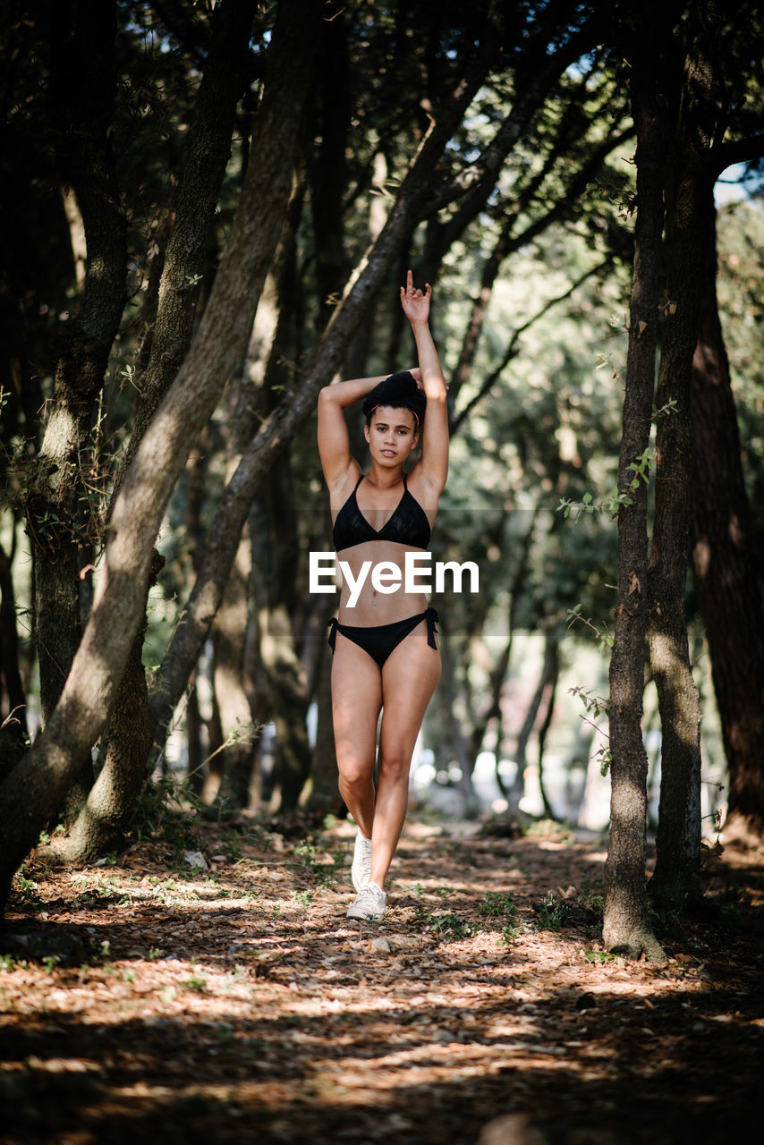 Portrait of young woman walking against trees in forest