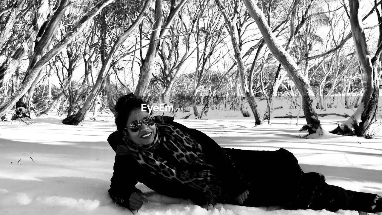 winter, cold temperature, snow, tree, black and white, one person, nature, monochrome, monochrome photography, warm clothing, clothing, plant, leisure activity, lifestyles, day, adult, land, full length, sitting, black, portrait, outdoors, footwear, young adult, beauty in nature, women, environment, bare tree, smiling, emotion