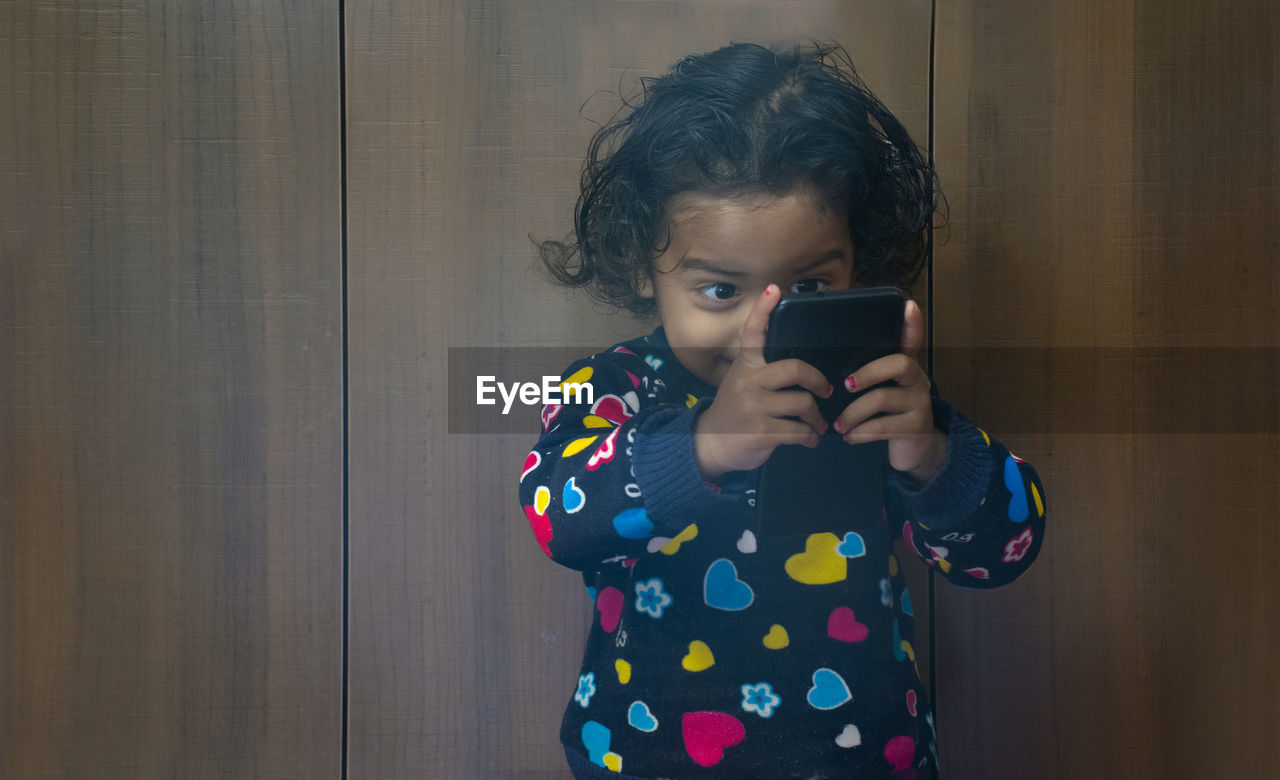 Close-up of girl holding smart phone against closet